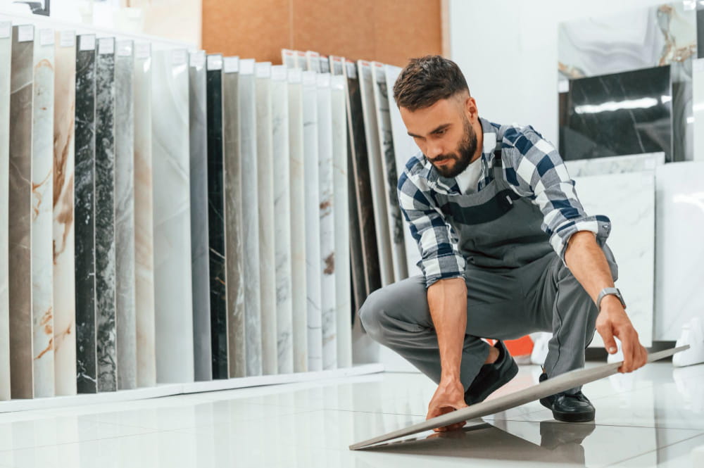 Un professionnel ou client accroupi comparant des dalles de carrelage grand format dans un showroom de revêtements